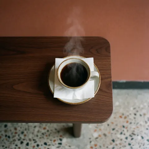 Steaming black coffee in a cup on a white napkin over a dark wooden table with a terracotta wall and terrazzo floor background