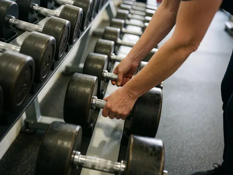 Close-up of adult hands adjusting dumbbells on a gym rack with rubber flooring and professional lighting