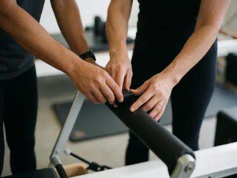 Two people adjusting the tension on a reformer in a yoga and pilates studio.