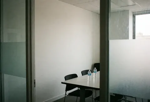 Spacious empty conference room featuring a table, chairs, water bottles, white walls, and glass partitions suitable for nonprofit organizations.