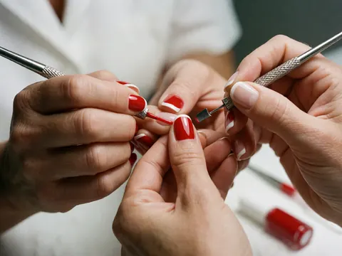 Close-up of a French manicure in progress featuring red and white nails, metal tools, and glossy polish on a clean background