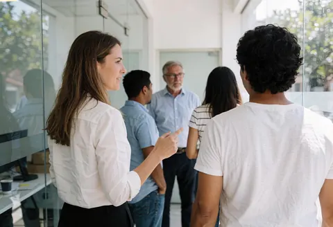 A woman guides a group through a modern office with glass walls.
