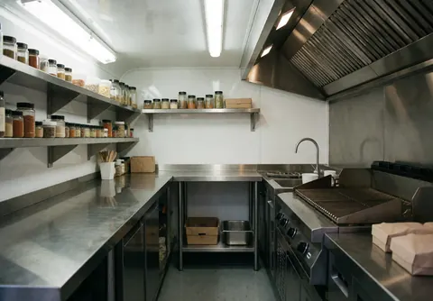 Bright interior of a food truck kitchen featuring a stove, spice shelves, and shiny stainless steel surfaces