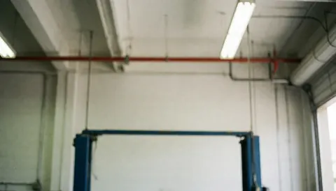 Blurred background of a mechanic shop with fluorescent lights, pipes, and metal structures, ideal for advertising text.