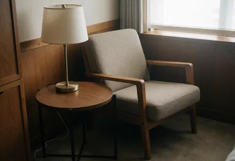 Comfortable wooden and fabric chair beside a round table and floor lamp in a warm office with wood walls and natural light