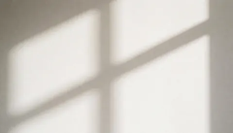 Soft shadow of a window blind cast on a light gray wall, providing a minimalist background for business presentations or websites.