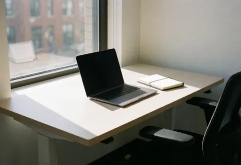 Modern workspace featuring an open laptop and notebook beside a window with natural light, an ergonomic chair, and a tidy professional atmosphere