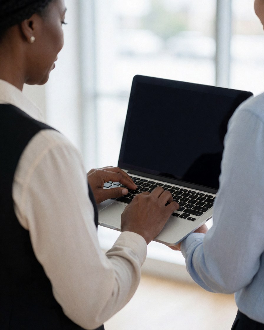 Two people collaborating on a laptop in a bright office setting.
