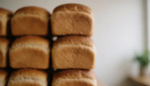 Stacked sliced bread loaves in a bakery with a blurred background and warm natural lighting, providing copy space for text.