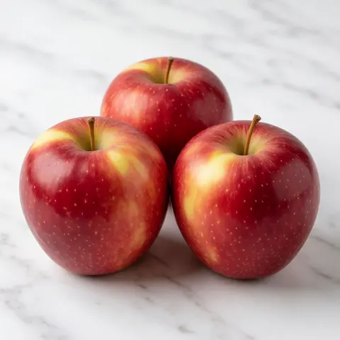 Three shiny red apples with yellow streaks resting on a polished white marble surface, suitable for grocery store product displays