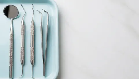 Sterile dental tools including a mirror, probes, and forceps arranged on a blue tray against a white background, suitable for dental clinic backgrounds.