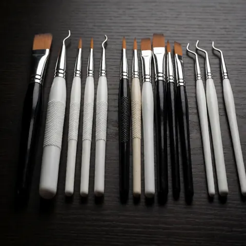 A row of professional nail art brushes and tools arranged on a dark wooden table with dramatic lighting and high contrast