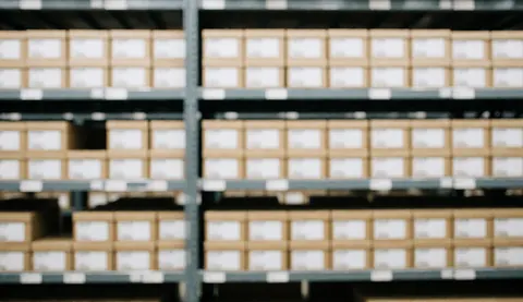 Out of focus background of organized warehouse shelves and stacked cardboard boxes suitable for logistics text overlay