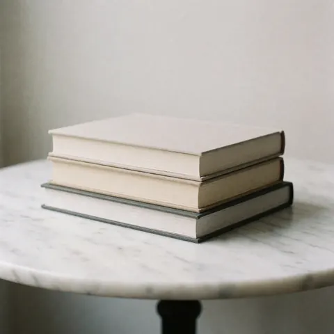 A stack of three books with smooth covers rests on a white marble table with gray veins.