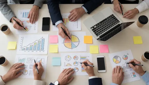 Close-up of hands sketching diagrams on paper during a business meeting with a laptop, phones, and sticky notes on the table