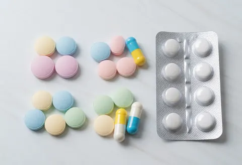 Assorted colorful tablets and capsules arranged on a white background, including a blister pack with white pills, ideal for pharmacy and healthcare product imagery.