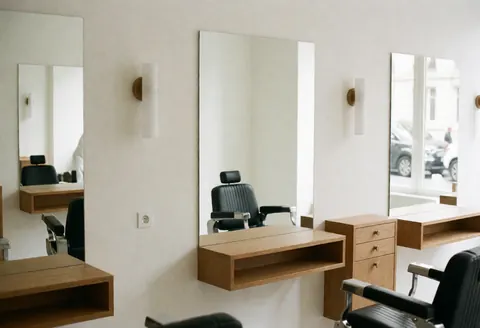 Minimalist barbershop interior featuring black chairs, mirrors, and wooden tables against white walls
