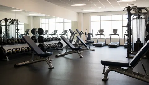 Empty modern gym interior featuring weight benches, dumbbells, and exercise machines for fitness training