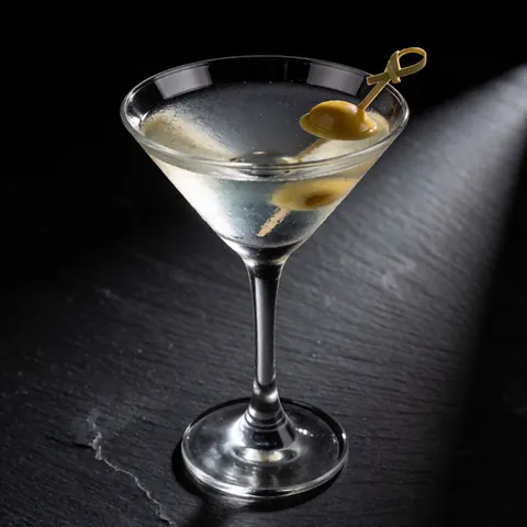 A martini with an olive in a cocktail glass on a dark stone table with dramatic lighting
