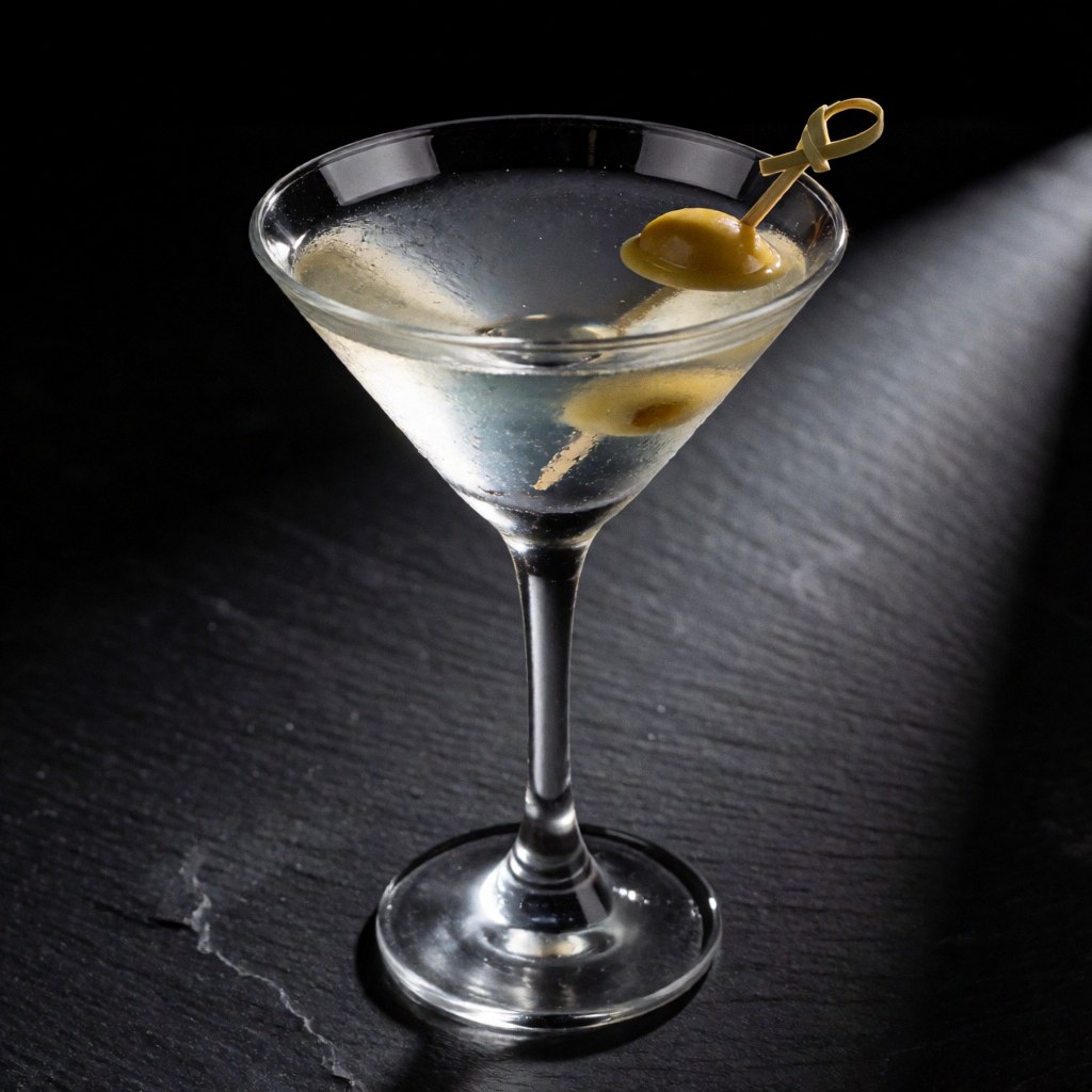 A martini with an olive in a cocktail glass on a dark stone table with dramatic lighting