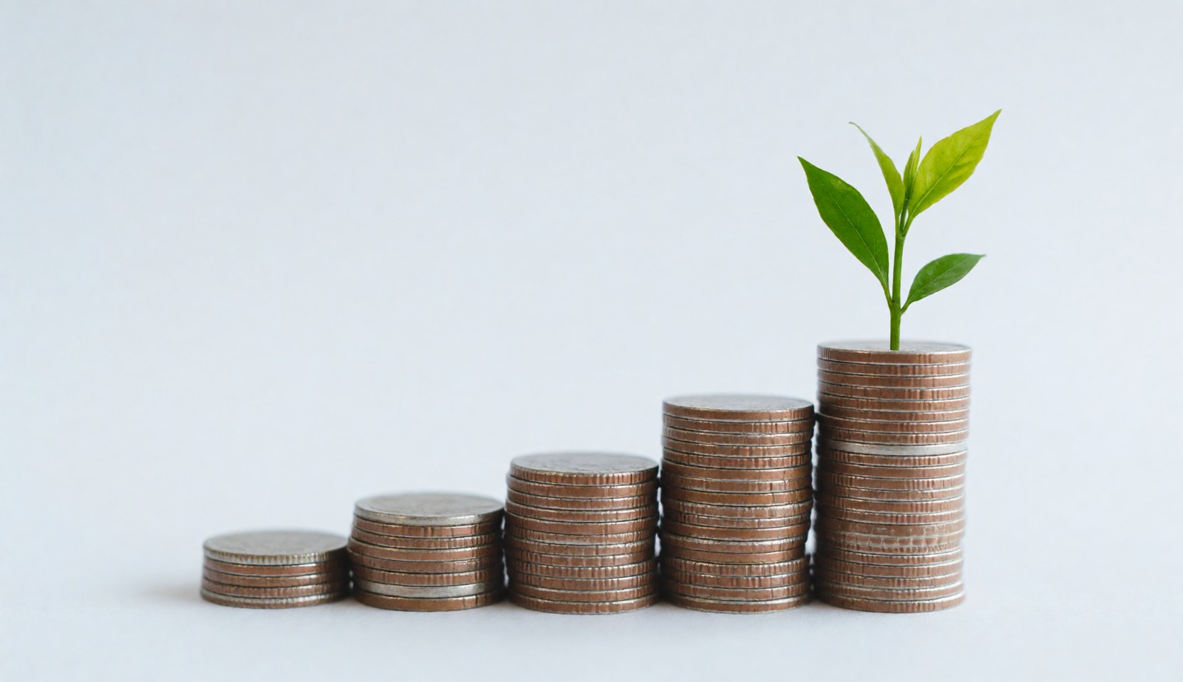 A stack of coins arranged in an ascending bar chart shape with a small green plant growing from the top coin, symbolizing financial growth and sustainable investment.