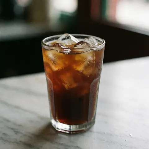 A glass of iced coffee with ice on a white and gray marble table.