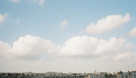 Blue sky with white clouds over the rooftops of a European city.
