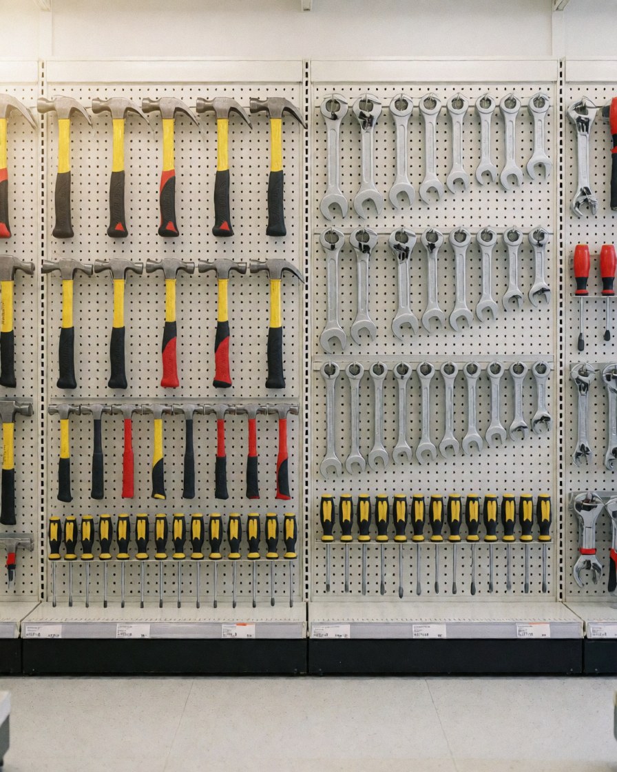 Various tools like hammers, wrenches, and screwdrivers hanging on a pegboard wall in a hardware store.