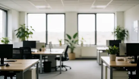 Blurred modern office with desks, computers, and plants.