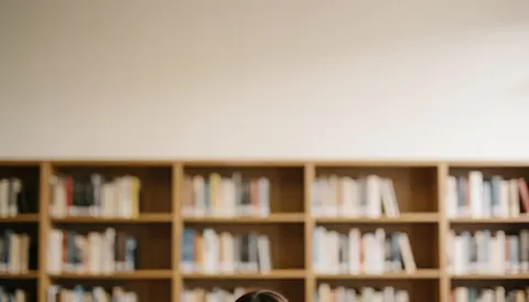 Person from behind in front of bookshelves in a library with warm light.