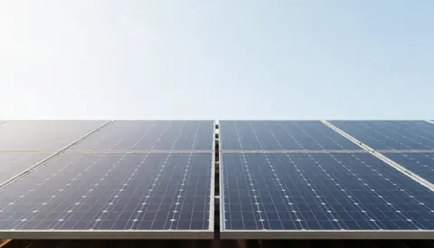 Clean energy solar panels installed on a roof under a clear blue sky, ideal for business text backgrounds.