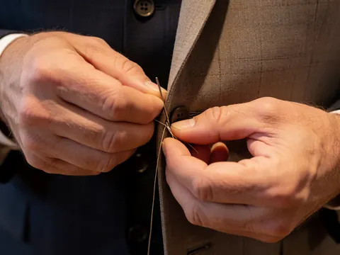 A man's hands sewing a button onto a plaid suit jacket.
