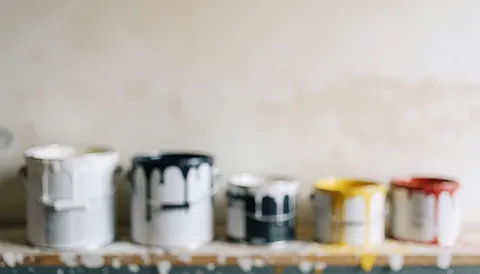 Paint cans with drips on a dirty shelf, white wall background with stains.