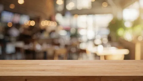 An empty wooden table set against a softly blurred restaurant interior, providing a warm and inviting background suitable for text overlays or food presentation.