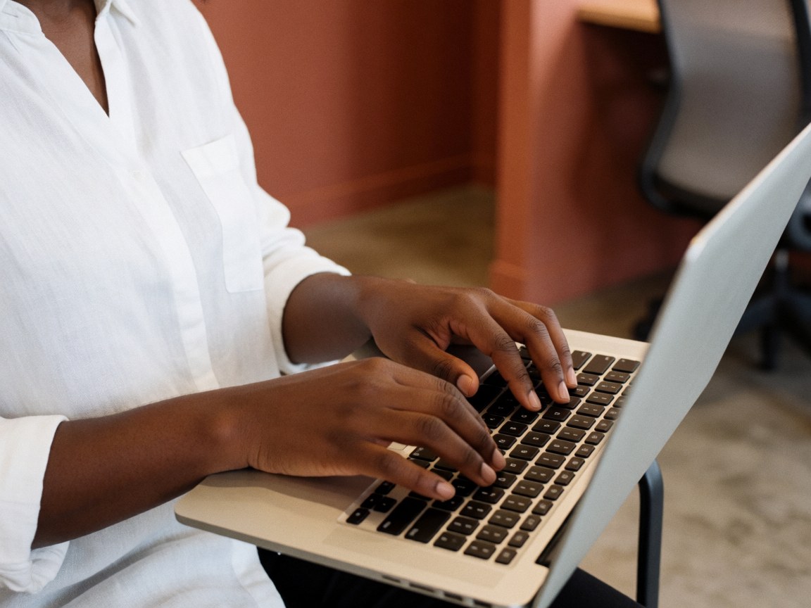 A person in a white shirt typing on a laptop computer in an indoor workspace.