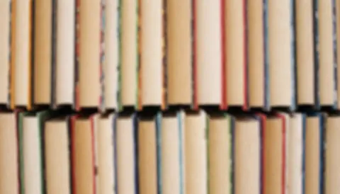 A stack of colorful books arranged in a row, creating a soft, blurred background texture suitable for text overlays and web design.