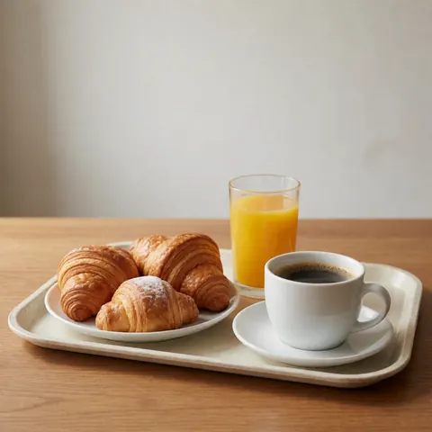 Breakfast served on a tray with croissants, black coffee and a glass of orange juice on a wooden table.