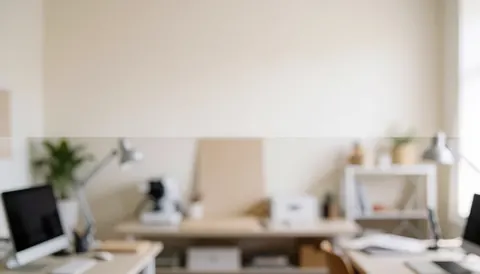 Blurred background of an office with desks, computers, and desk lamps.
