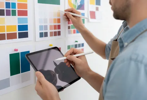 A designer with a tablet and digital stylus choosing color palettes on a wall with color samples.