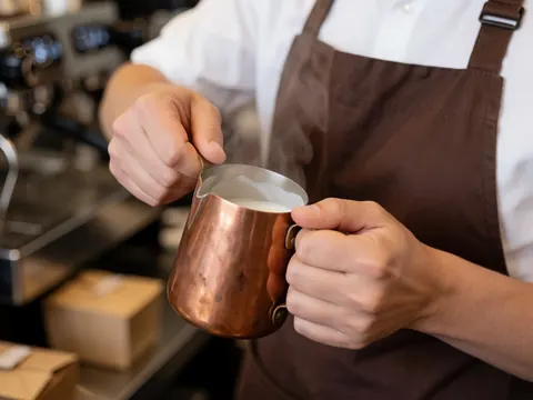 Barista warming milk in a copper pitcher in a café.