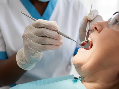 Dentist with white gloves examines patient's mouth with dental tools in a clinic.