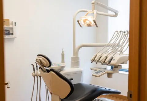 Empty dental operating room with chair, light, and medical equipment, viewed from the hallway.