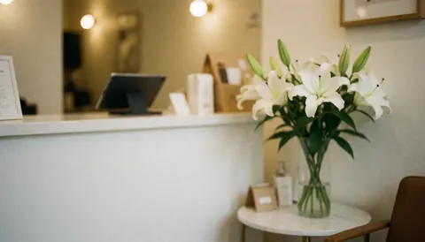Hair salon reception desk featuring a vase of white lilies, a tablet, and a chair in a warm, welcoming setting ideal for service text backgrounds.