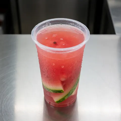 A plastic cup filled with fresh watermelon juice and rinds sits on the counter of a food truck, looking refreshing and appetizing.