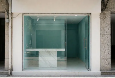 Clean and welcoming entrance of a modern aesthetic clinic featuring teal walls, a marble table, and large glass windows.