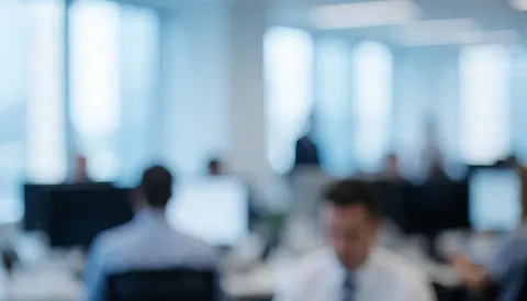 A soft focus background of a contemporary corporate office space featuring desks, chairs, and large windows with bright natural light.