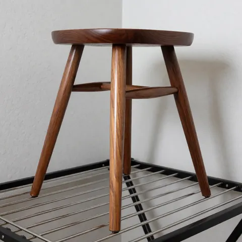 Restored wooden chair with glossy finish, visible legs, placed on a metal shelf against light gray walls with professional lighting