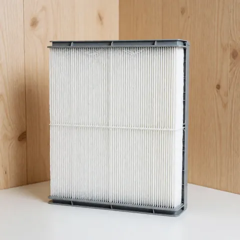 Close-up of a new white rectangular air filter placed on a wooden surface, ready for installation in a residential HVAC system or fan unit.