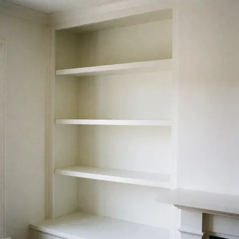 White built-in cabinet with three empty shelves, white walls, natural lighting, polished finish, ideal for interior design services.