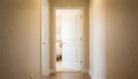 A residential hallway featuring textured beige walls and a slightly ajar white door, illuminated by warm light, suitable as a background for text overlays.